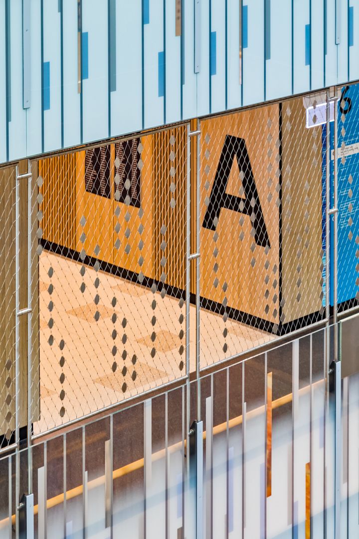 Close-up of a colourful building facade with blue panels, metal mesh screening and a large black letter A on an orange wall.