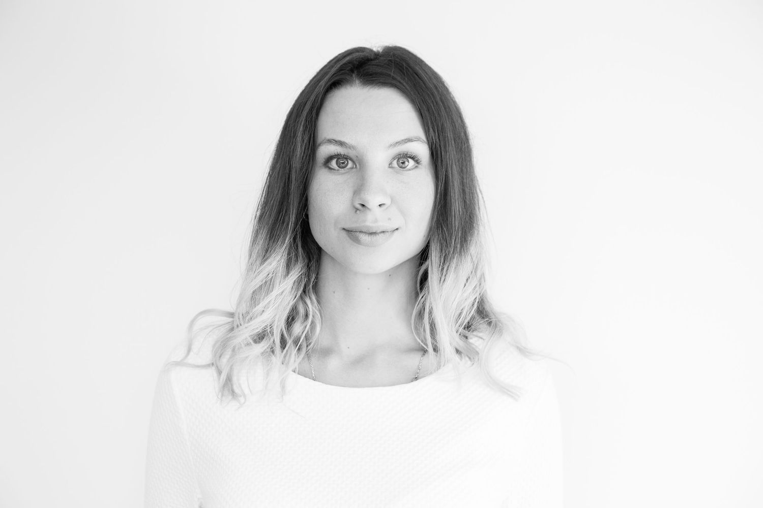 A black and white portrait of a young woman with long ombre hair looking calmly at the camera against a plain background.