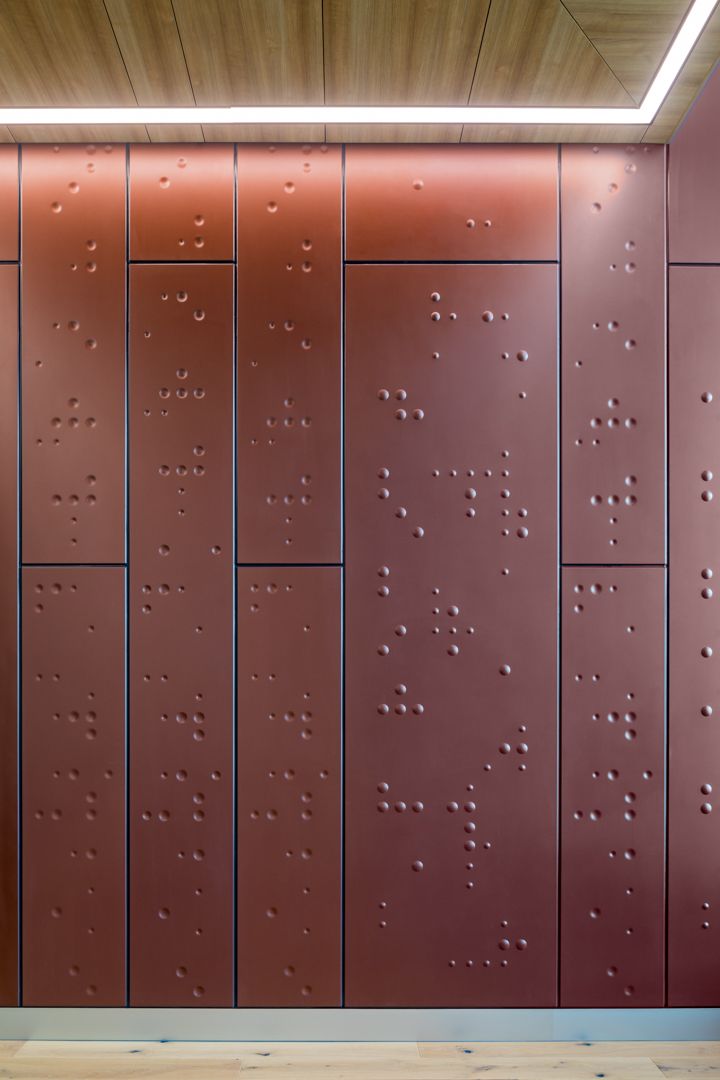 Copper-toned wall panels with raised braille-style dots beneath a linear ceiling light and timber ceiling.