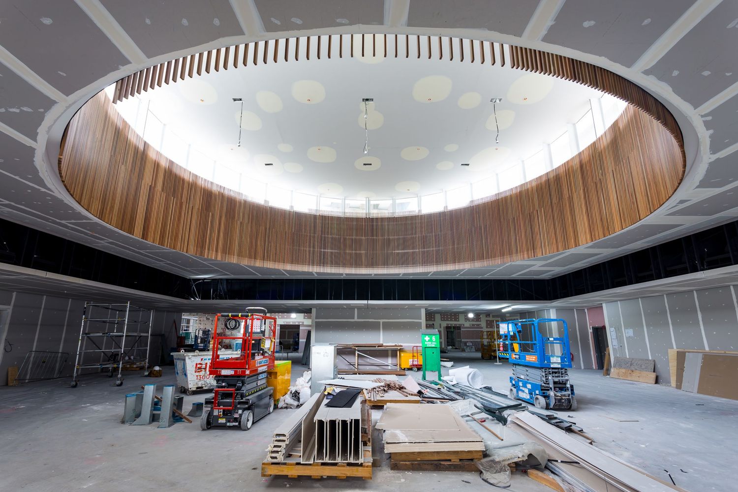 Unfinished interior with a large circular timber-clad ceiling void and construction equipment on the floor below.