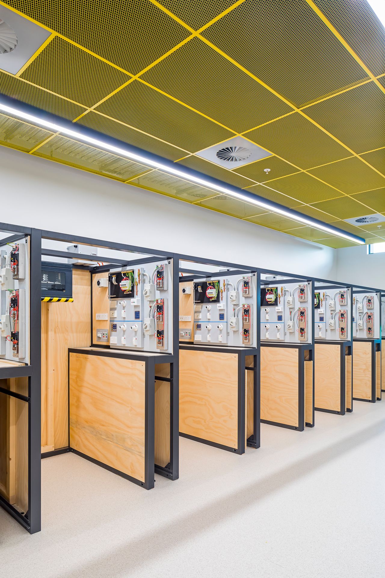 Modern electrical training workshop with rows of wired practice stations under a yellow perforated metal ceiling.