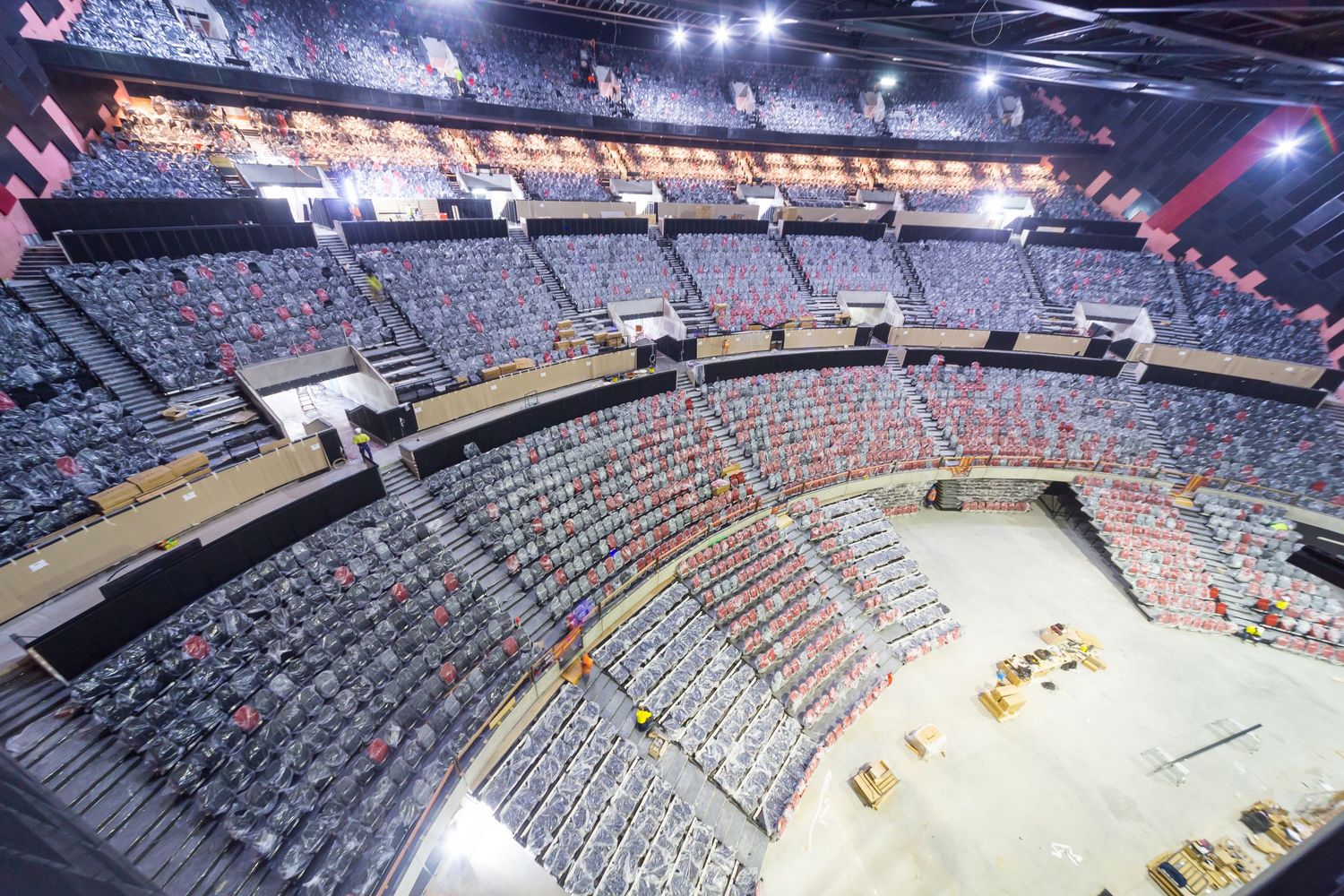 Elevated view of an indoor arena under construction showing tiered seating bowl, luxury suites, and a bare event floor with equipment.