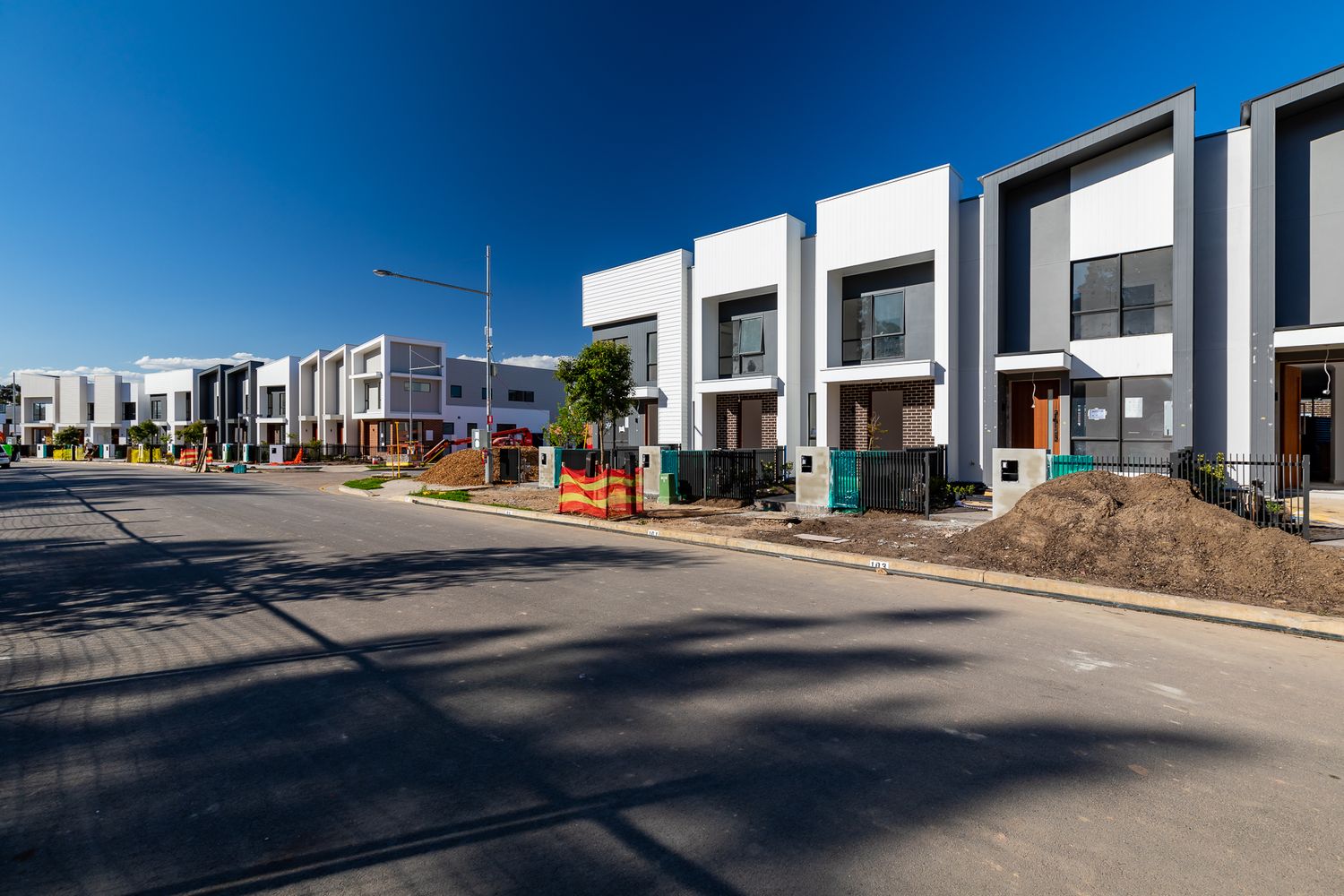 New modern townhouses lining a quiet street in a residential development, with construction materials and dirt mounds in front.