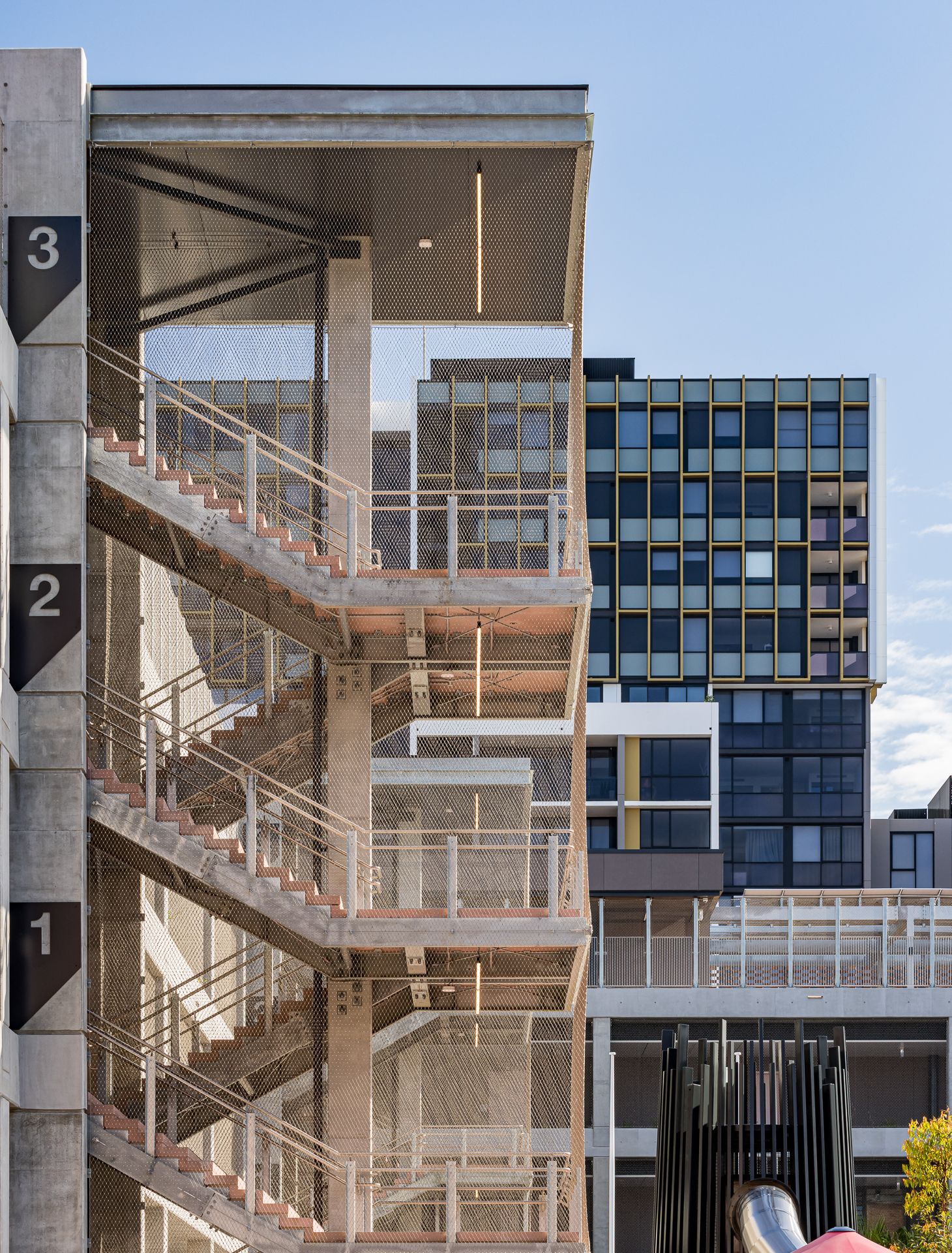 Open concrete stairwell with level numbers one to three overlooking a modern high-rise apartment building with a glass facade.