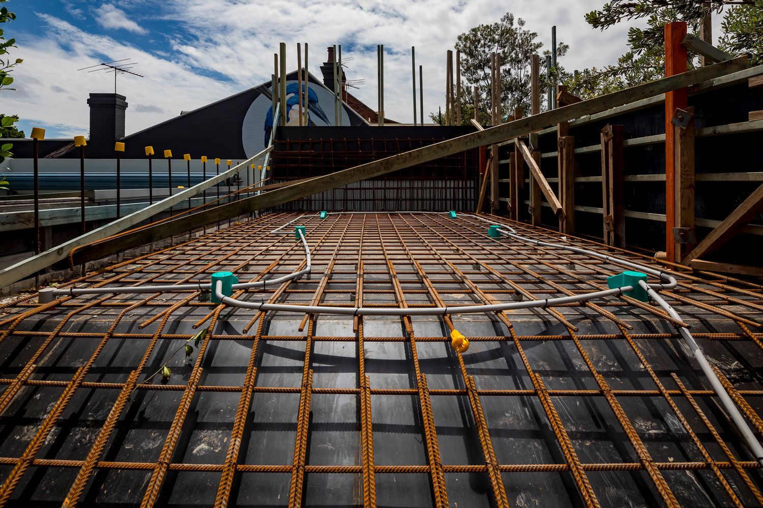 Steel reinforcement mesh with green fittings laid across a concrete slab formwork at a residential construction site.