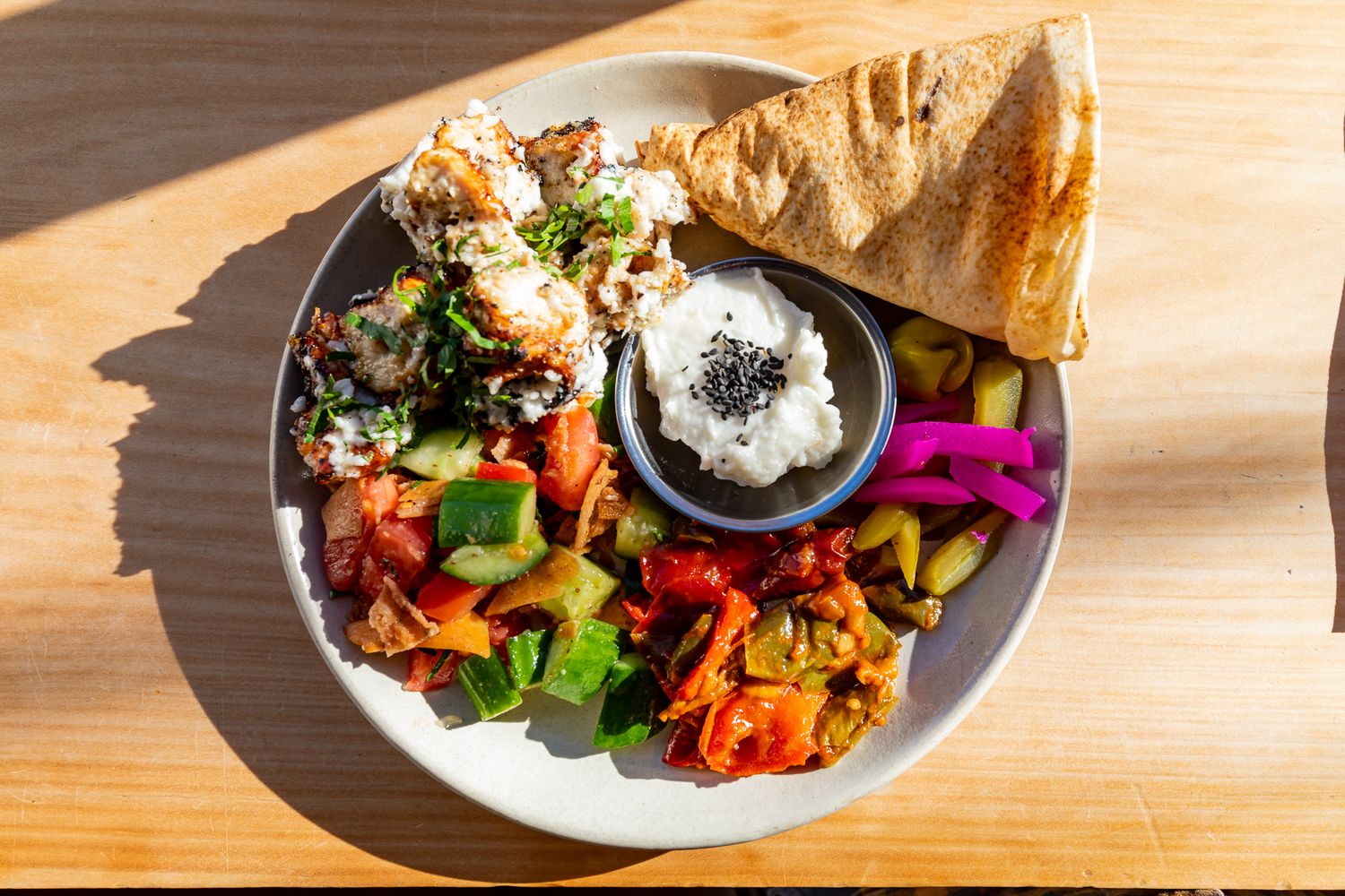 Mezze plate with hummus, tabbouleh, diced vegetable salad, pickled turnips, and pita bread on a sunlit wooden table.