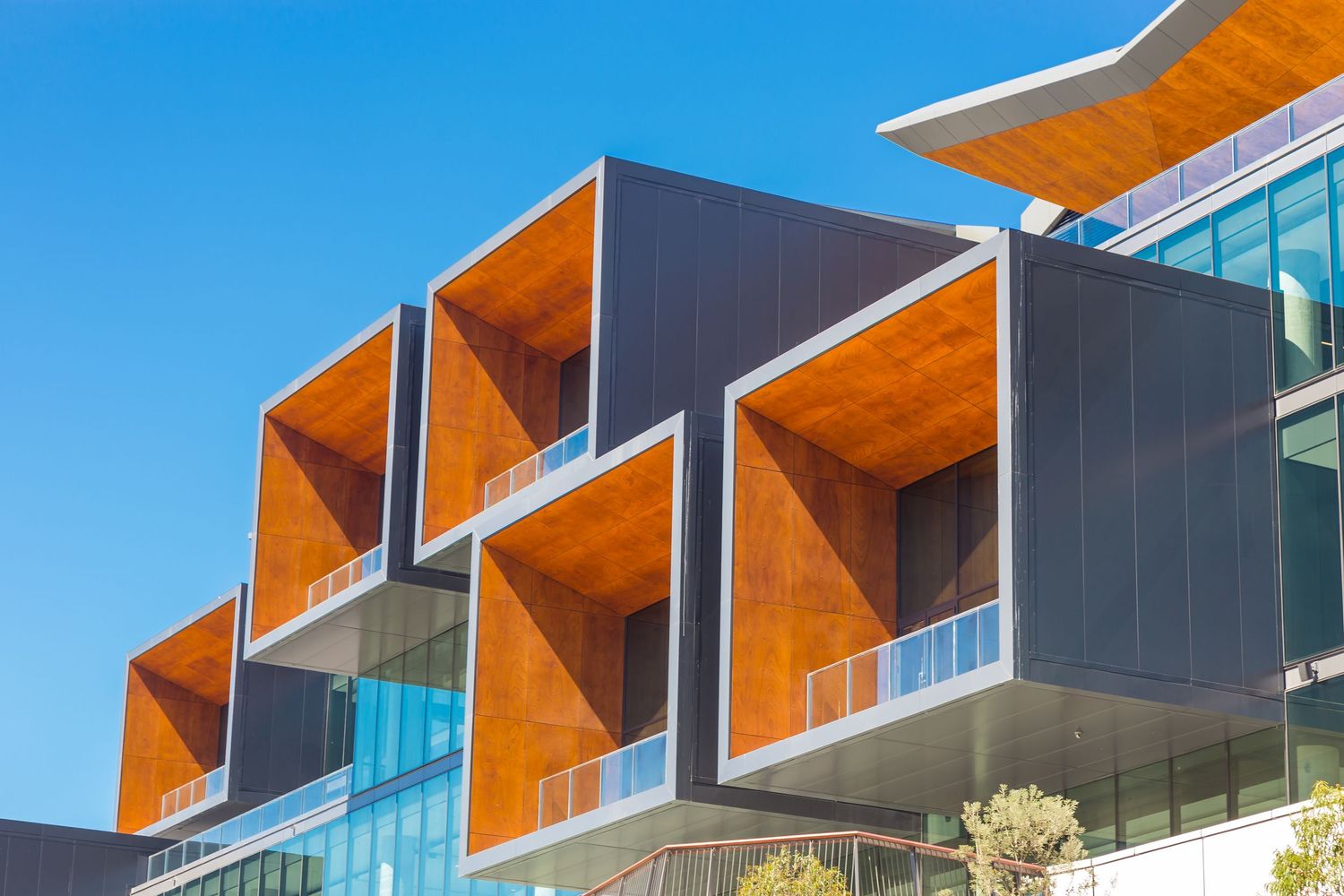 Close-up of ICC Sydney facade featuring stacked timber-lined balconies, dark metal cladding and glass under a bright blue sky.