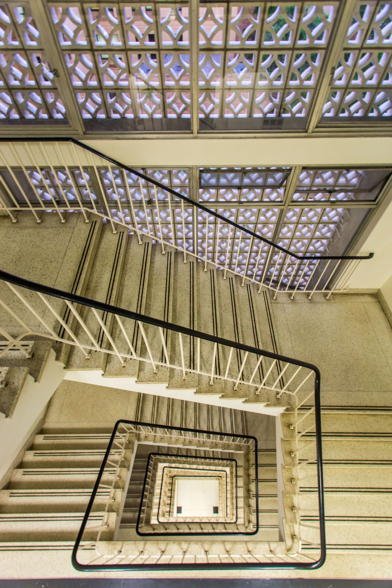 Overhead view of a mid-century modern spiral staircase with black railings and a decorative geometric breeze block screen.