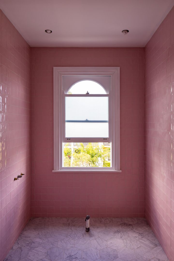 Pink tiled bathroom with an arched sash window, marble floor and soft natural light.