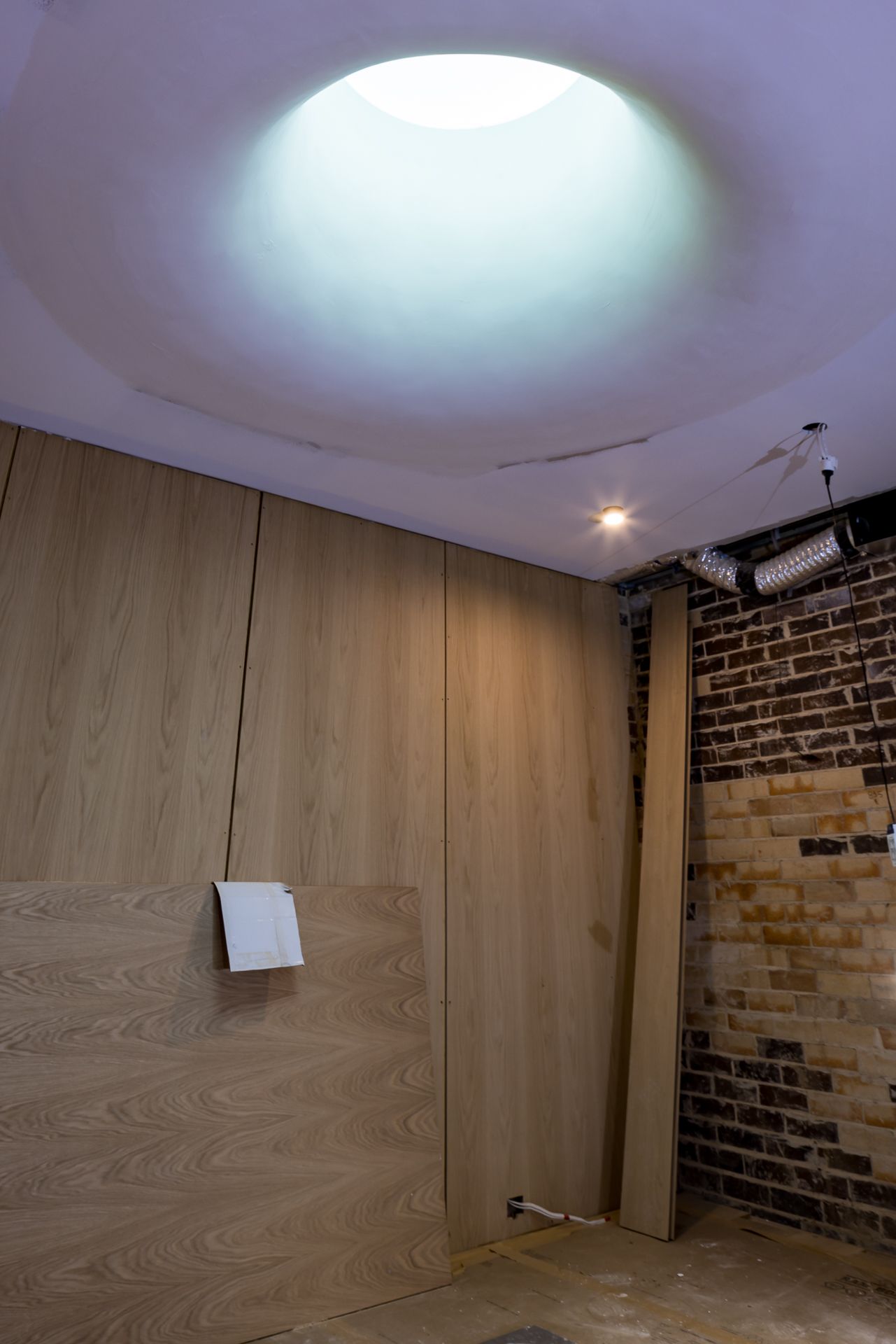 Room under renovation featuring oak wall panelling, a round skylight, recessed lighting and an exposed brick wall.