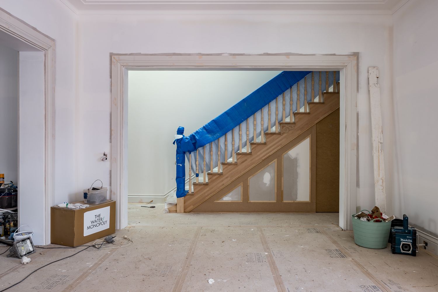 Staircase with a blue protective cover and white balusters seen through an open doorway in a home under renovation.