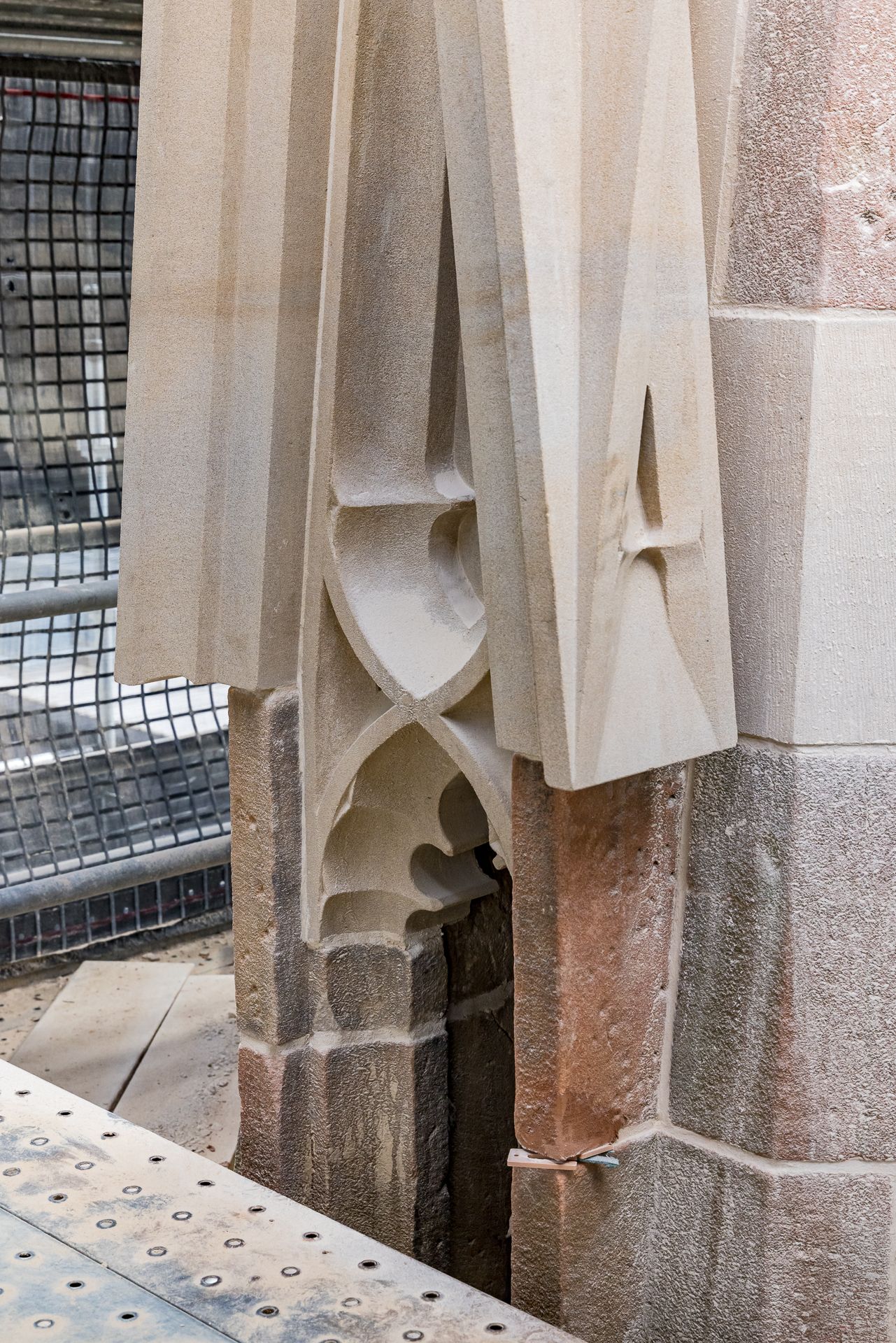 Newly carved pale sandstone pinnacle with Gothic tracery rests against weathered stone blocks inside a scaffolded building.
