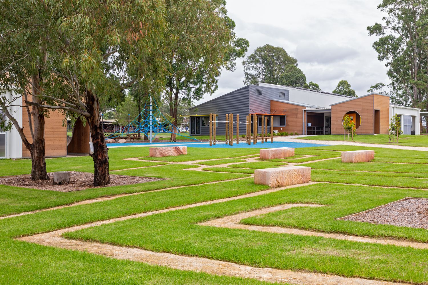 Landscaped garden with green lawn, winding sandstone paths and stone blocks in front of a modern brick and timber building.