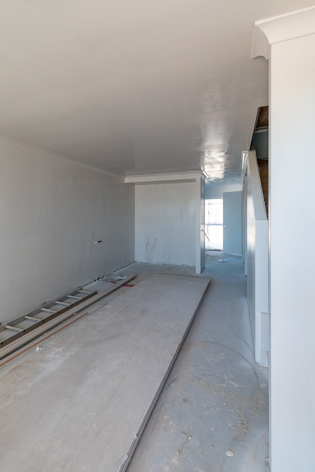 Unfinished townhouse interior with plastered walls, bare concrete floor, a ladder and a staircase under construction.