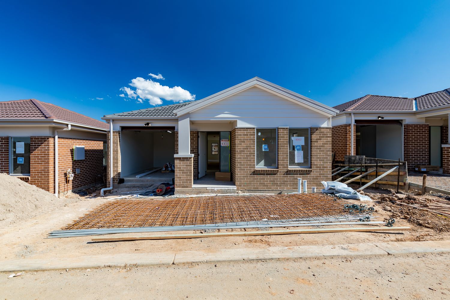 New brick home under construction with a front porch, garage, and reinforcing mesh laid in the front yard beneath a blue sky.