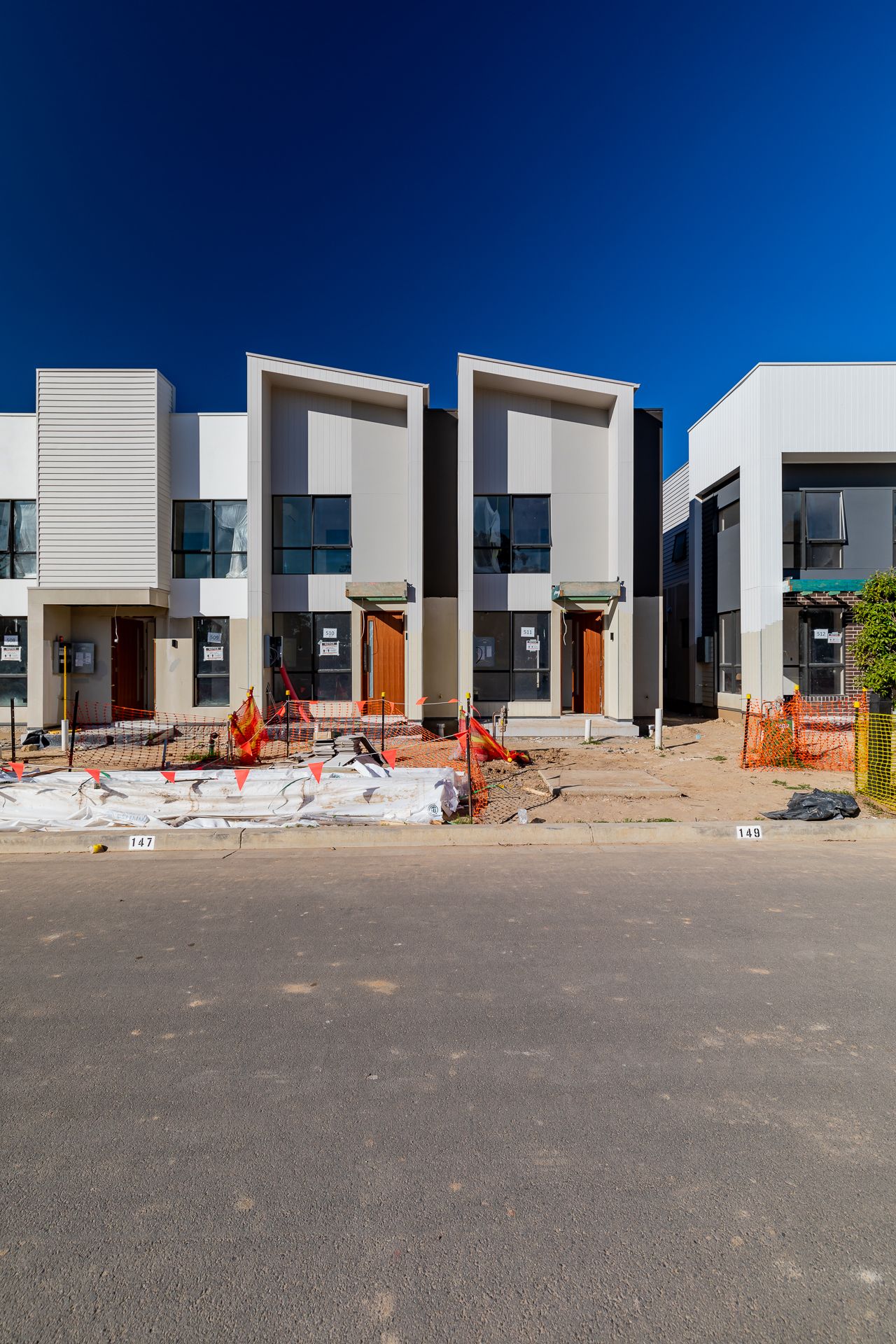 Row of modern two-storey townhouses with white and grey facades nearing completion beside a construction site and dirt road.
