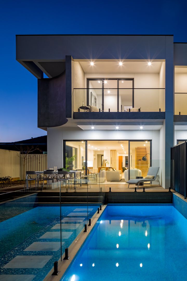Contemporary two-storey home at dusk with glowing interiors, a glass-fenced swimming pool and stepping stone pathway.