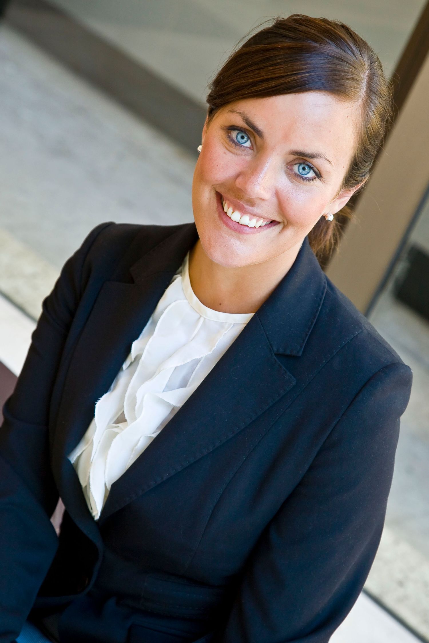 Smiling woman with blue eyes and her hair pulled back wears a navy blazer over a white ruffled blouse in a professional headshot.