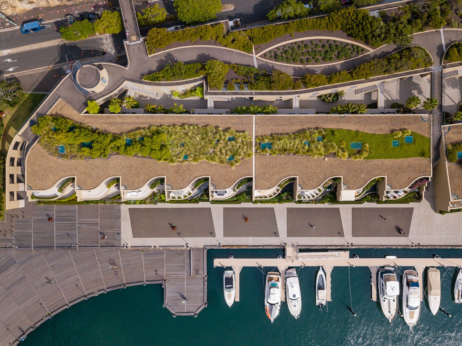 Aerial view of a terraced waterfront building with green roof gardens above a marina filled with moored boats.