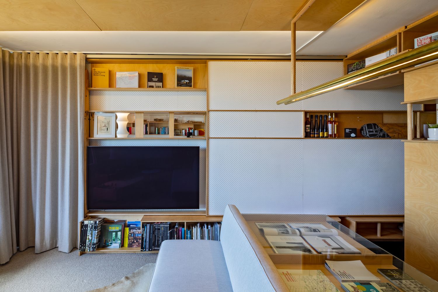 Sliding white perforated panels half-conceal a TV and display shelves in a stylish wood-accented apartment.