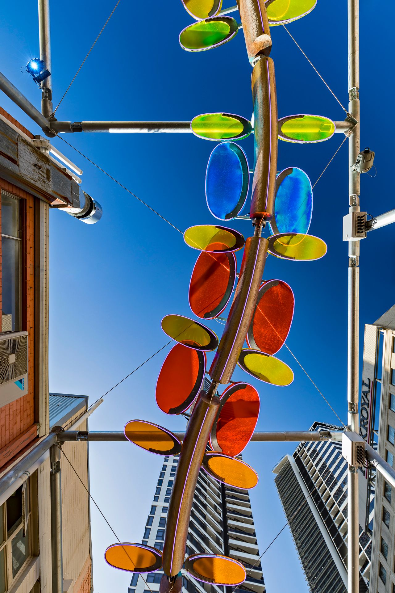 Colorful blue, yellow and orange discs on a curved metal sculpture hang overhead between city high-rises.