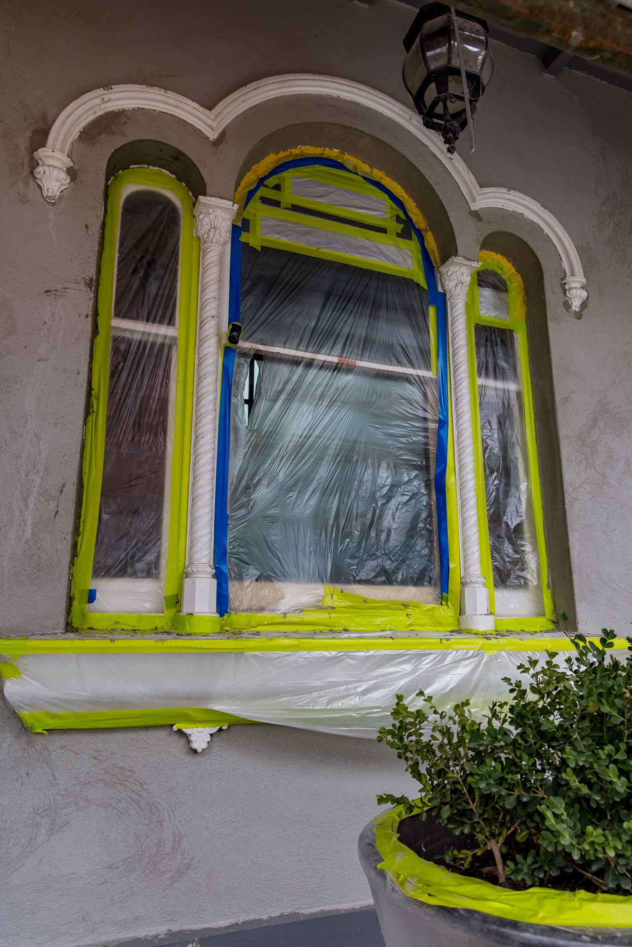 Heritage window with ornate plaster arch and columns, masked in yellow and blue tape and plastic sheeting for painting.
