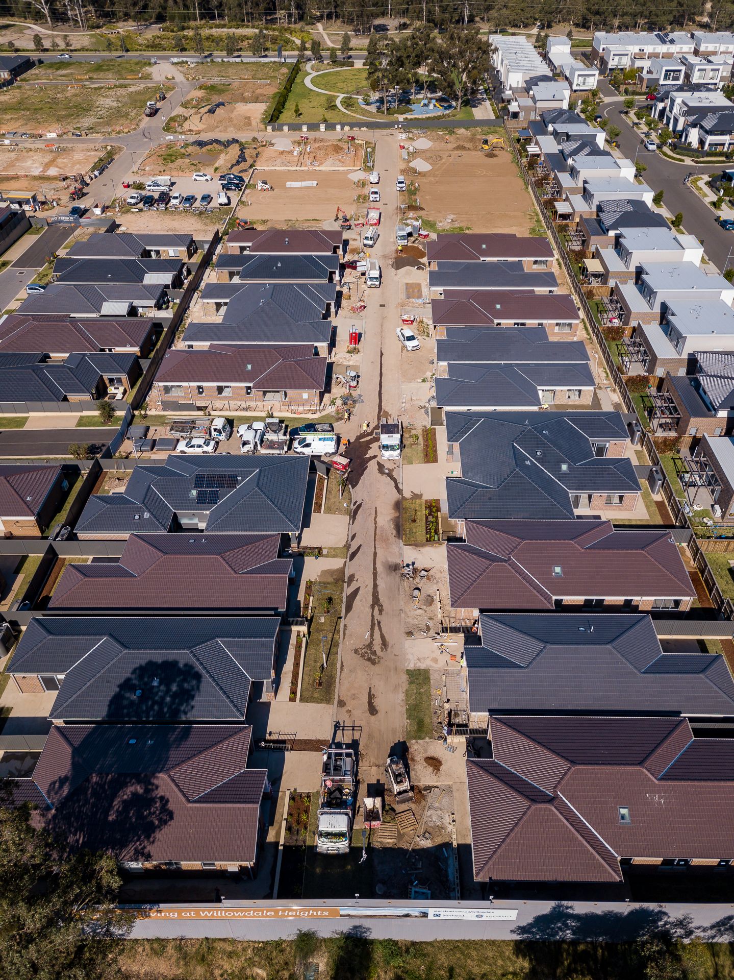 Aerial view of a new residential subdivision with dark-roofed homes, unpaved streets and construction vehicles on vacant lots.