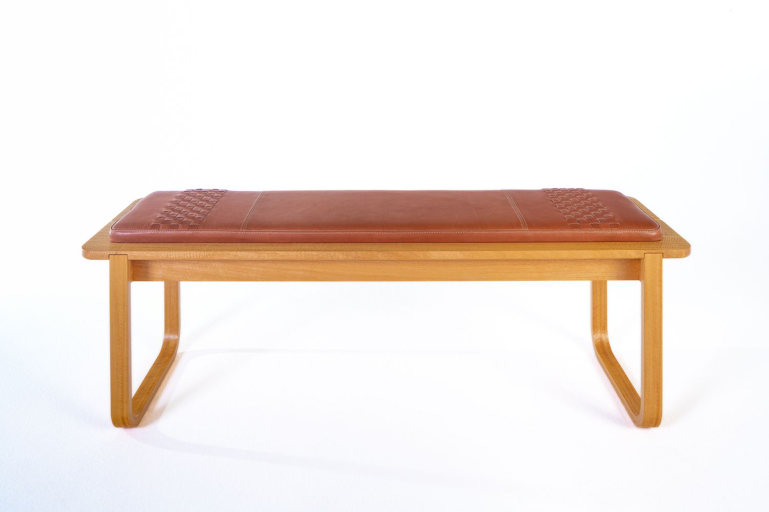 Minimalist oak bench with a tan leather woven cushion and curved wooden legs, photographed against a clean white background.