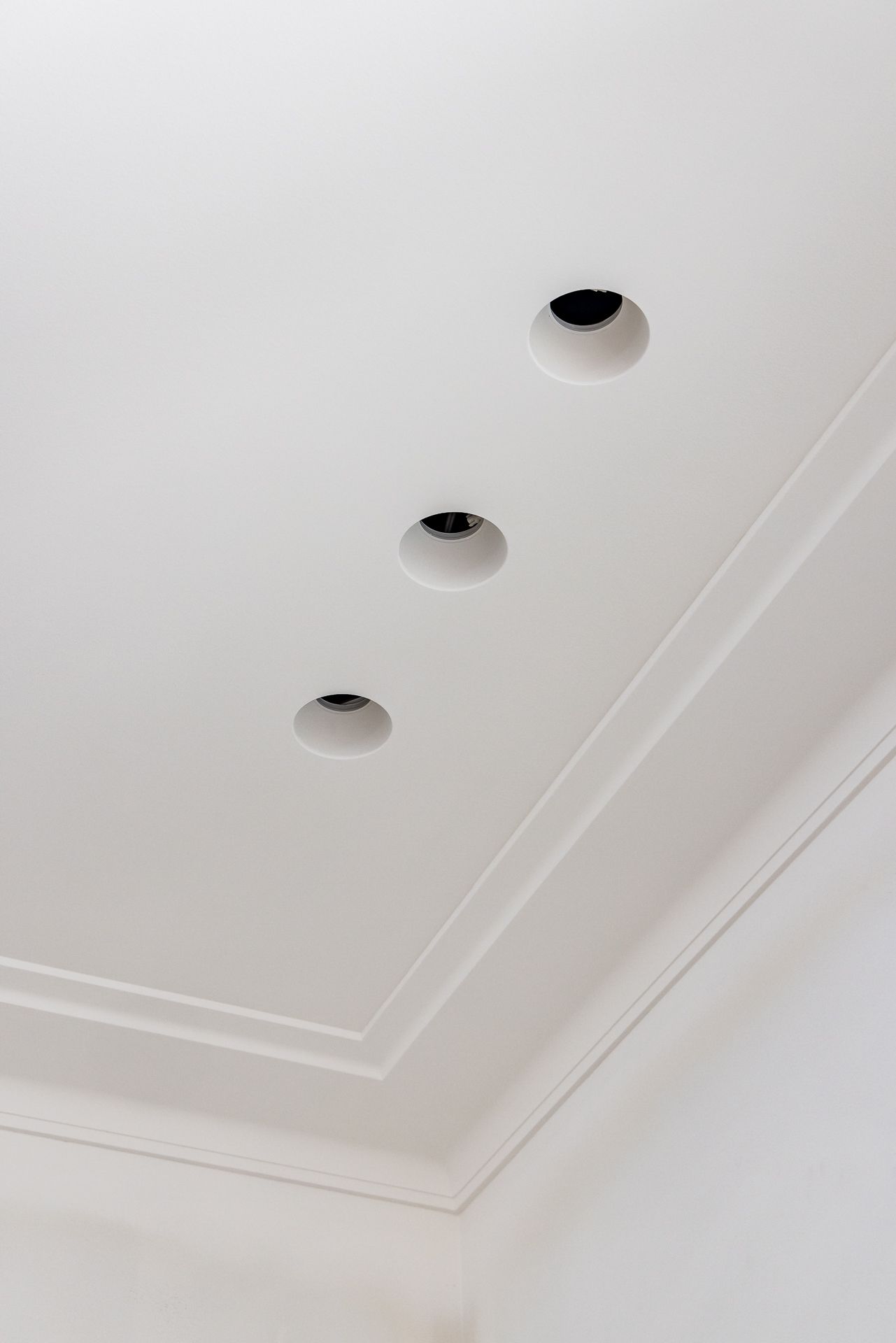 White ceiling with ornate cornice molding and three recessed downlights in a freshly finished room.