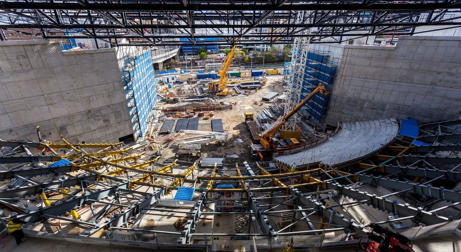 Wide view of a large construction site with cranes, steel framing and concrete walls inside a major building under construction.