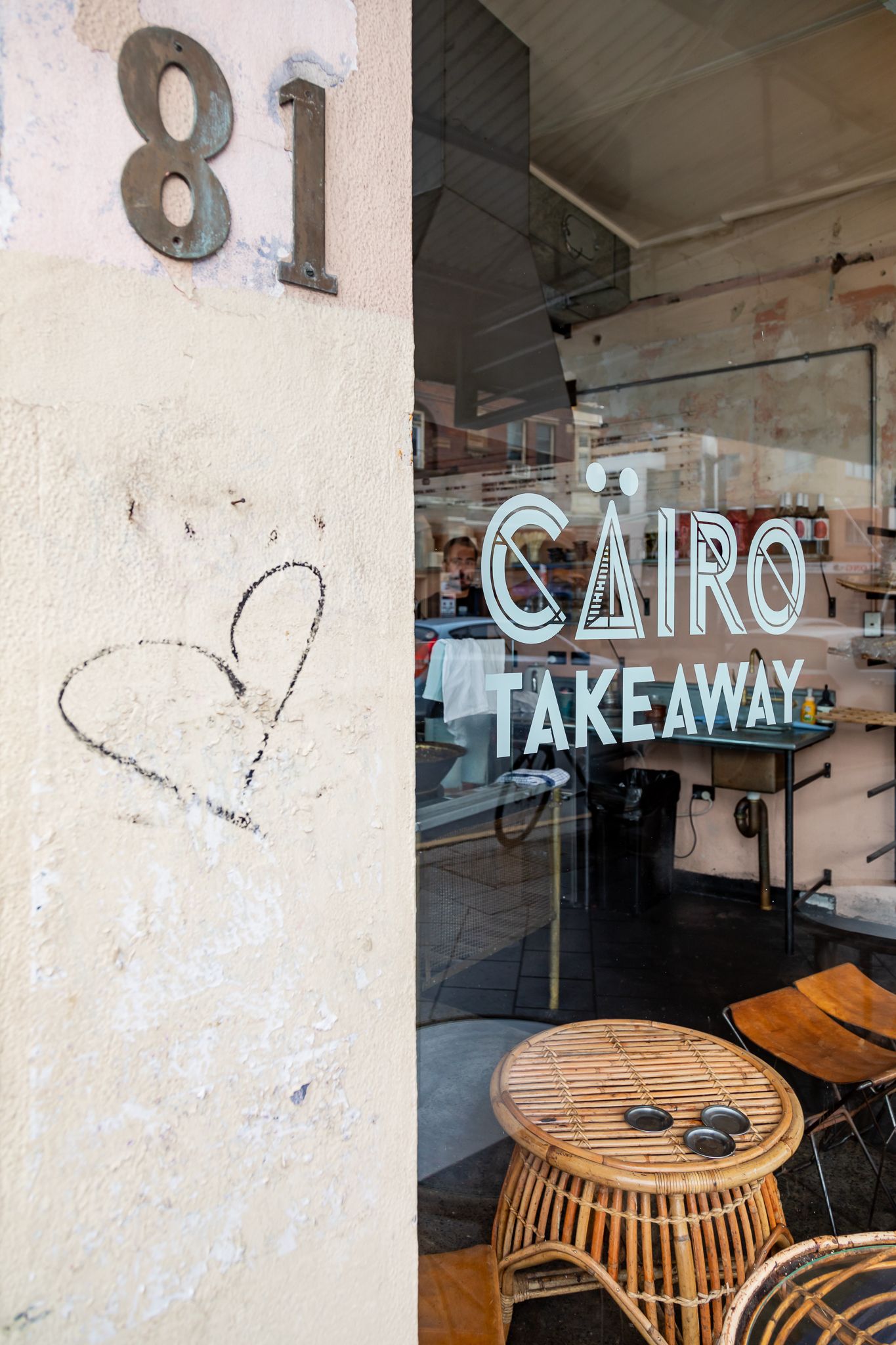 Cairo Takeaway shop window with white lettering, rattan stools and a hand-drawn heart graffiti beside the number 81.