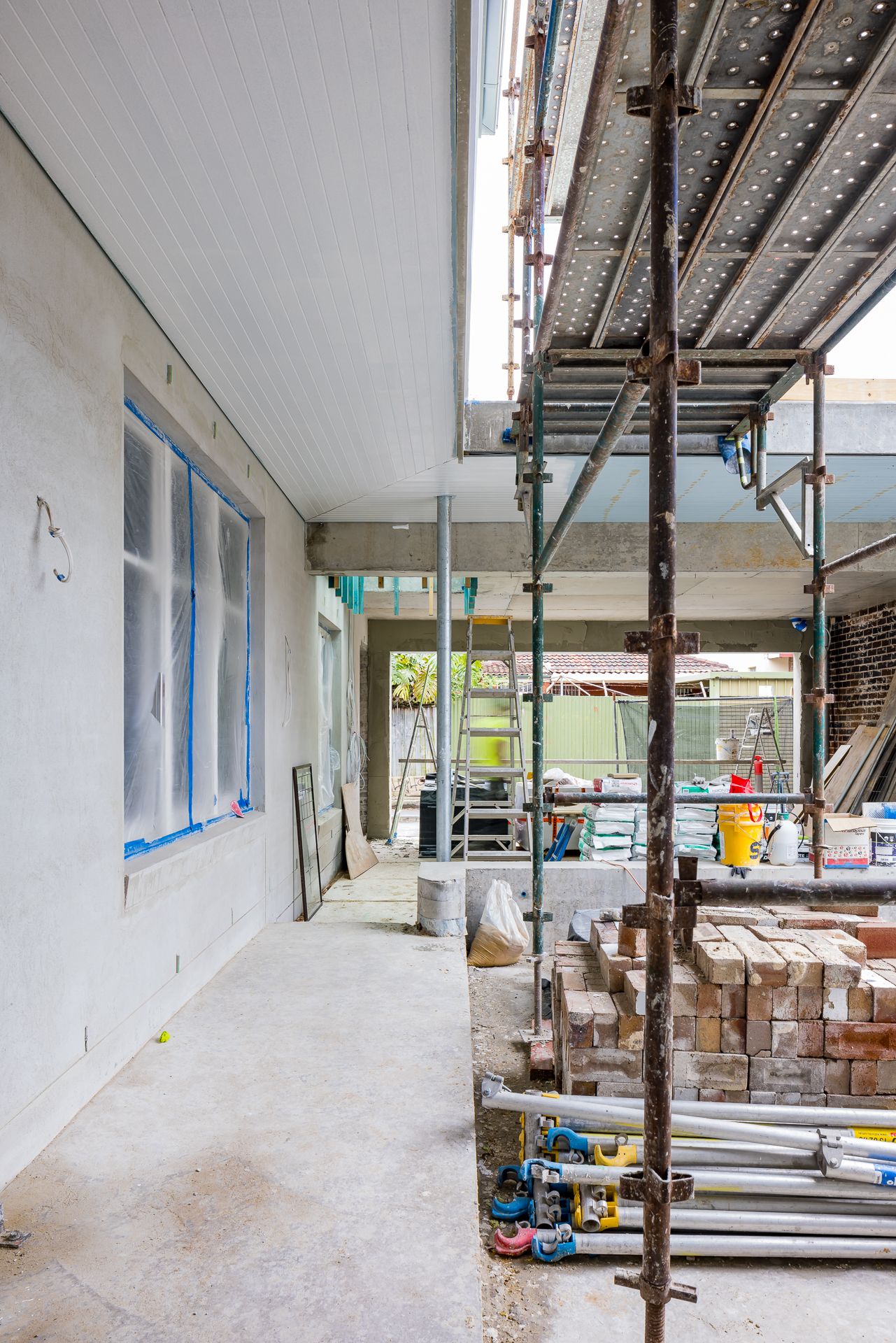 Construction site beside a house with scaffolding, stacked bricks and covered windows during an exterior renovation project.