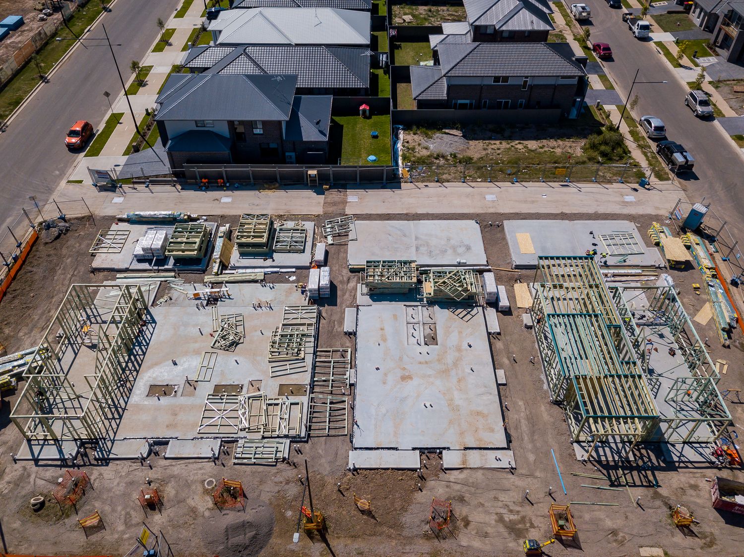 Aerial view of house construction with timber frames and concrete slabs beside completed homes in a new housing development.