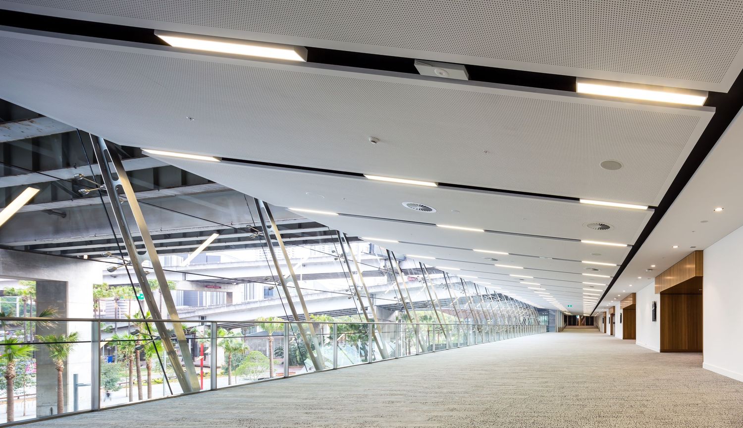 Spacious glass-walled concourse with a sleek white ceiling, recessed lighting and carpeted floor inside a modern convention centre.