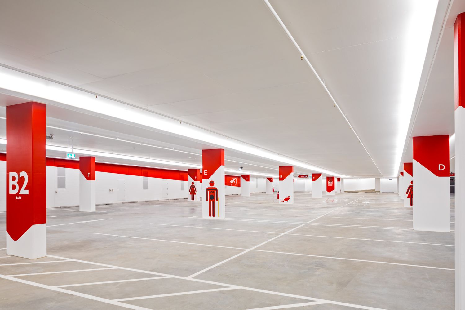 Bright underground car park with white ceiling lights, red and white numbered columns and level B2 signage.