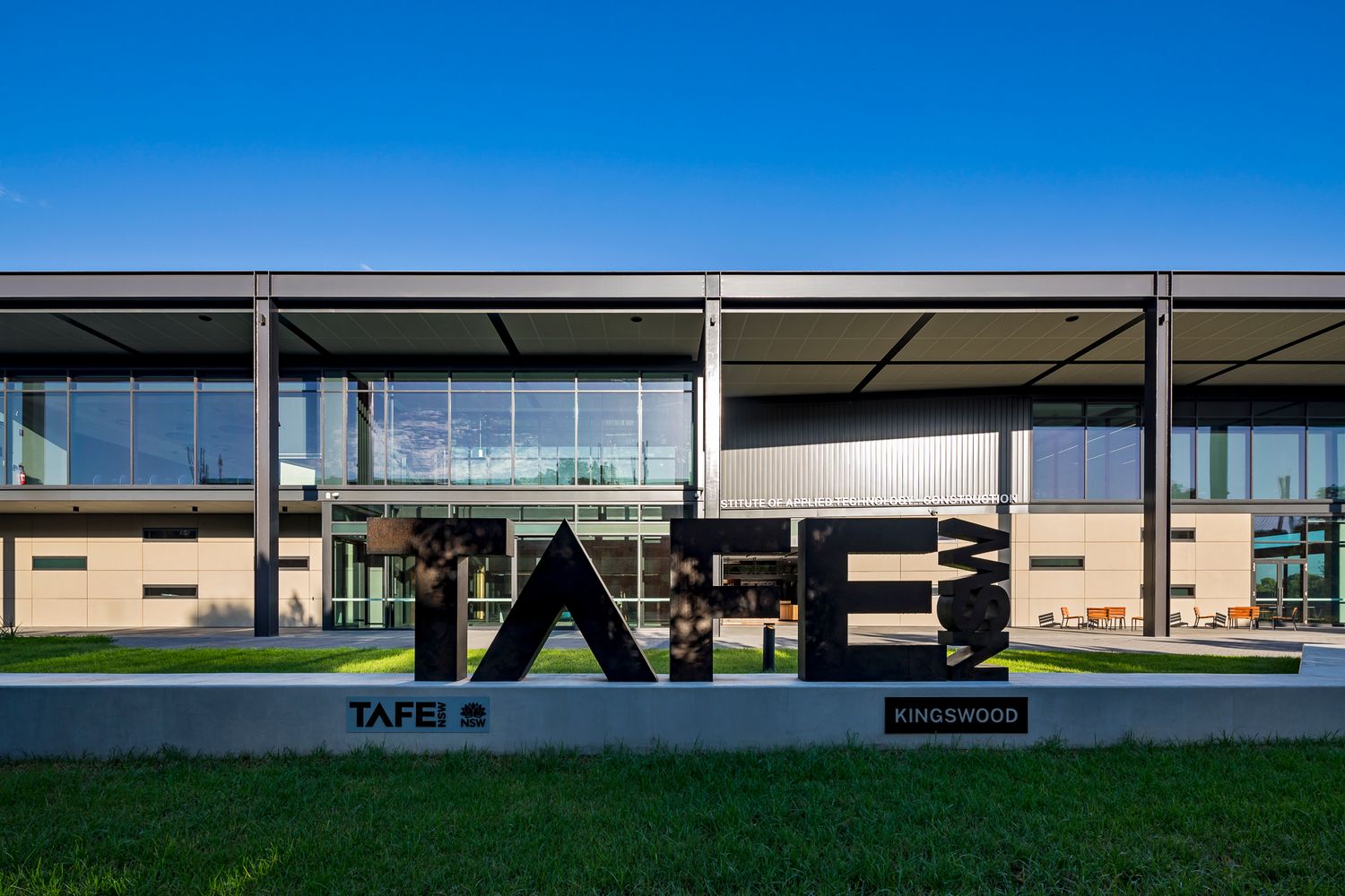 Modern TAFE Ringwood campus building with large glass facade and bold 3D TAFE lettering on a landscaped lawn under a clear blue sky.