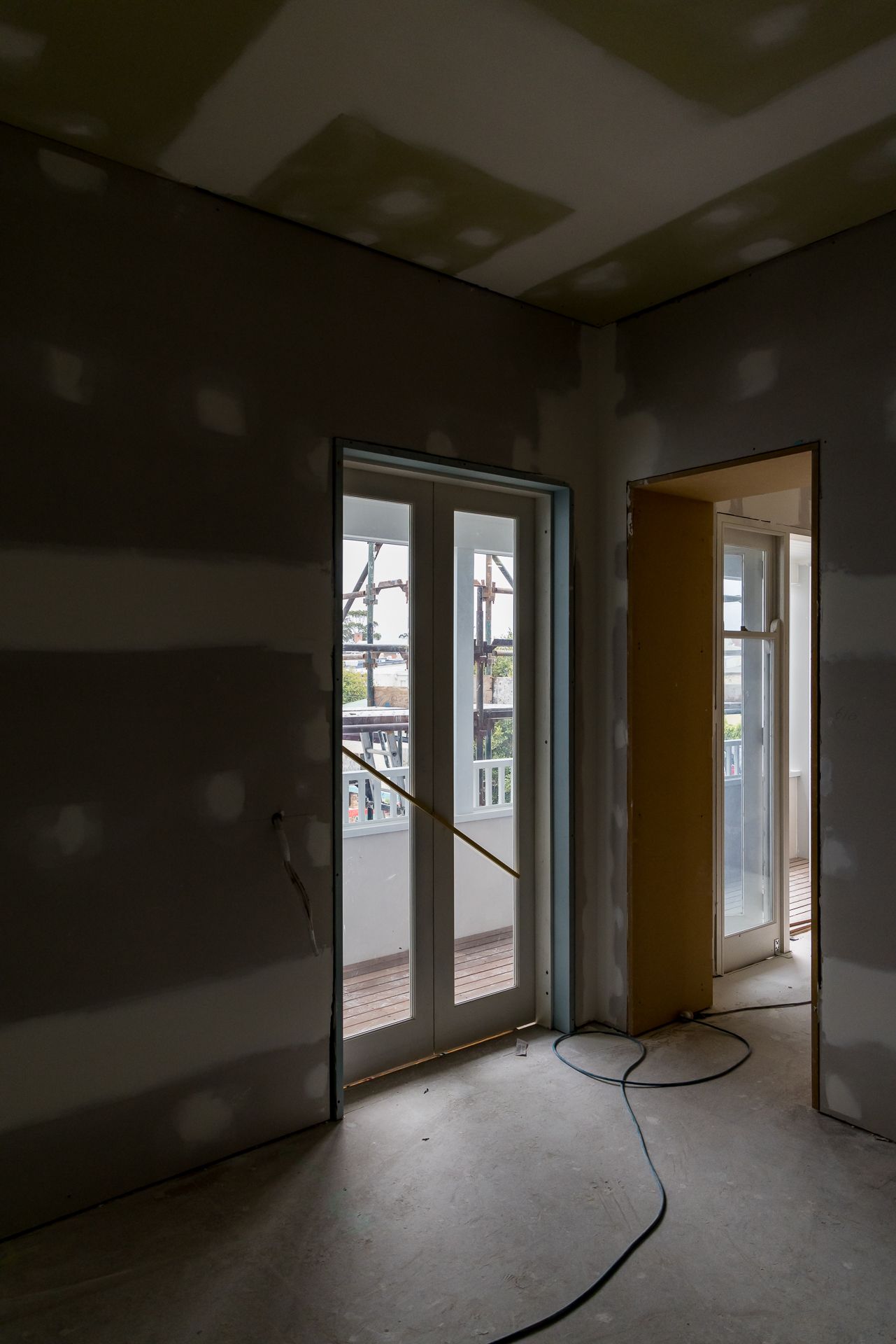 Renovation in progress inside a room with raw plasterboard walls and French doors opening to a balcony.