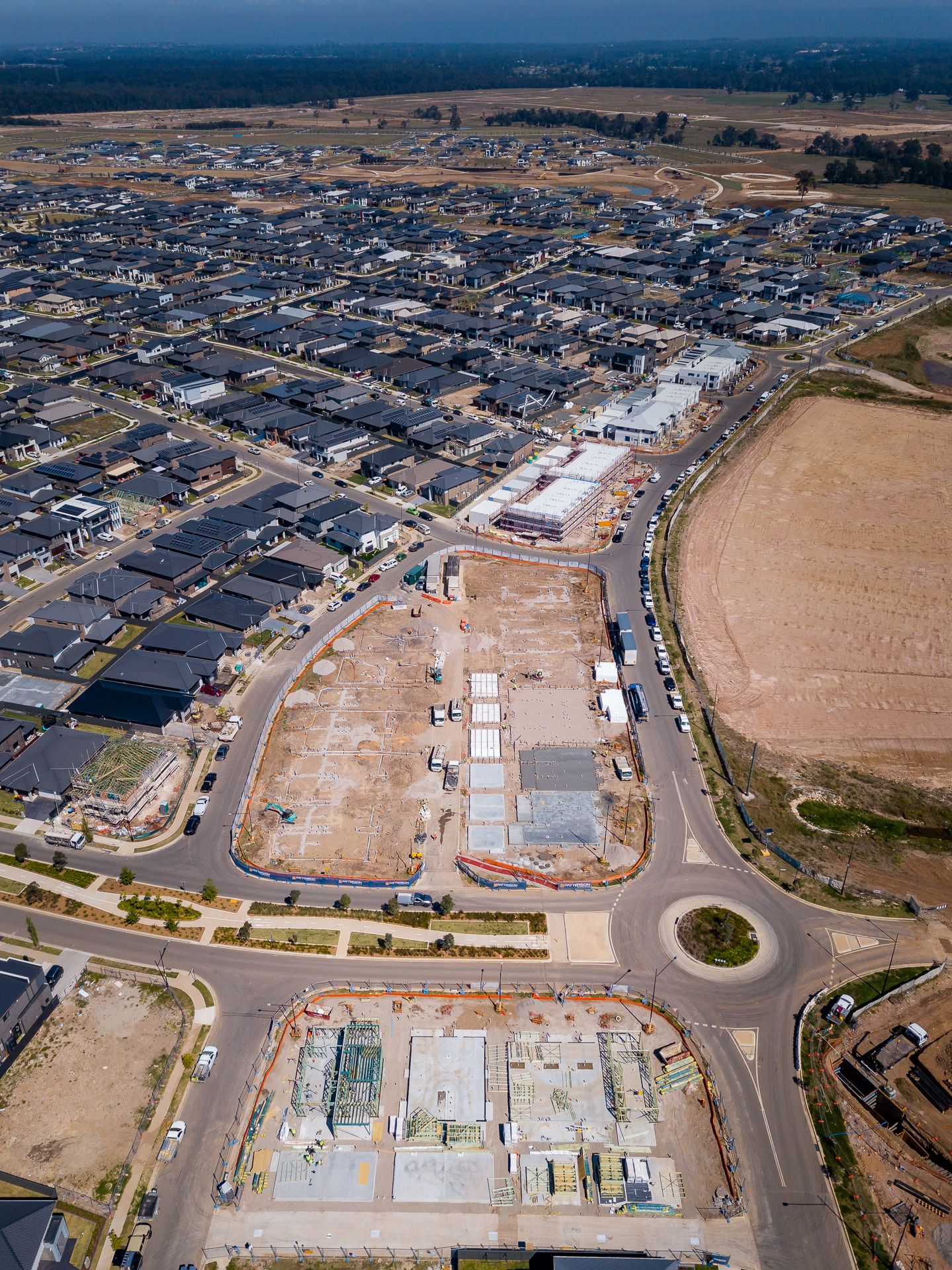 Aerial view of a new suburban housing estate with rows of completed homes, roundabouts and vacant construction lots under development.