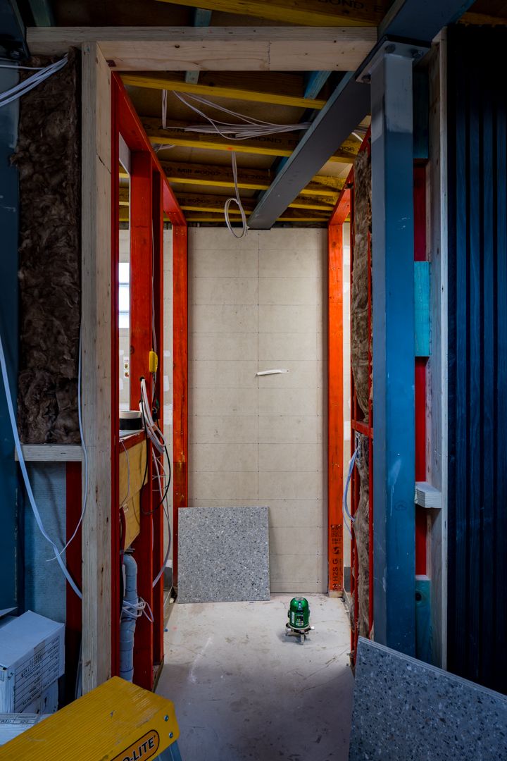 Interior of a building under construction showing exposed orange and blue framing, insulation, wiring and a green laser level on the floor.