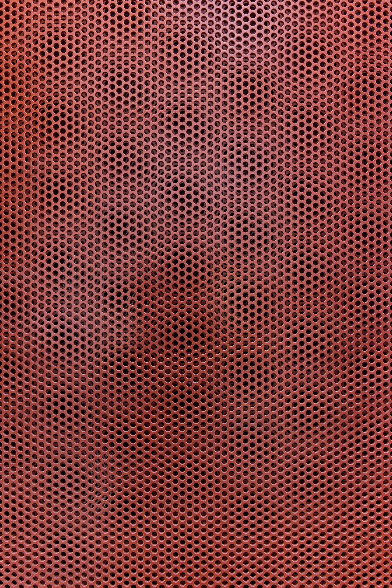Close-up of a red perforated metal panel with a dense, even pattern of small round holes.