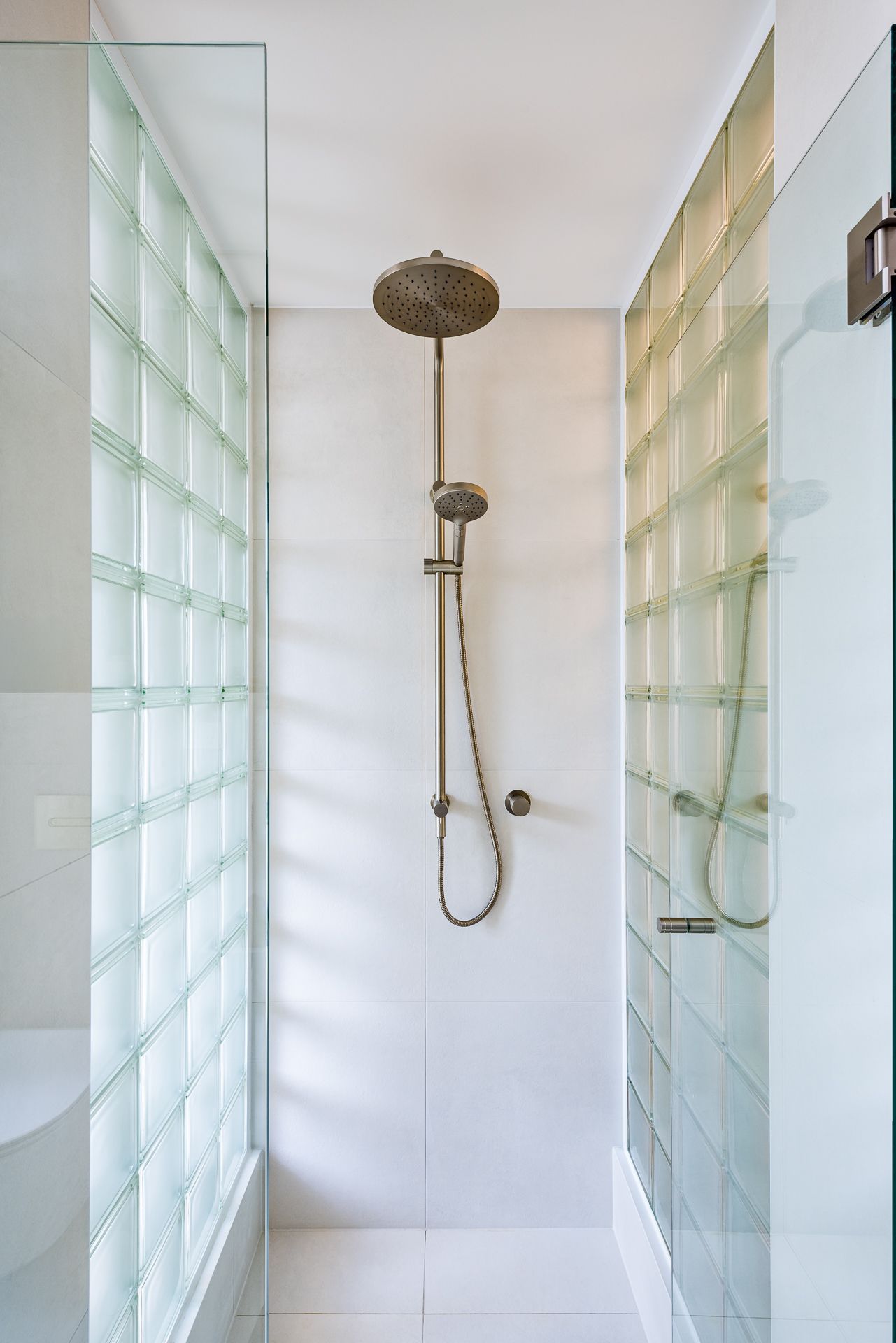 Walk-in shower with brushed nickel rain showerhead and handheld sprayer enclosed by translucent glass block walls.