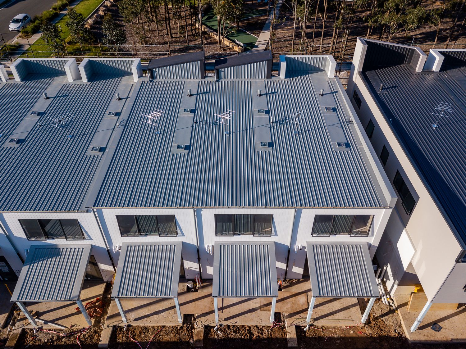 Aerial view of a new townhouse row with corrugated metal roofs, skylights and small covered patios.