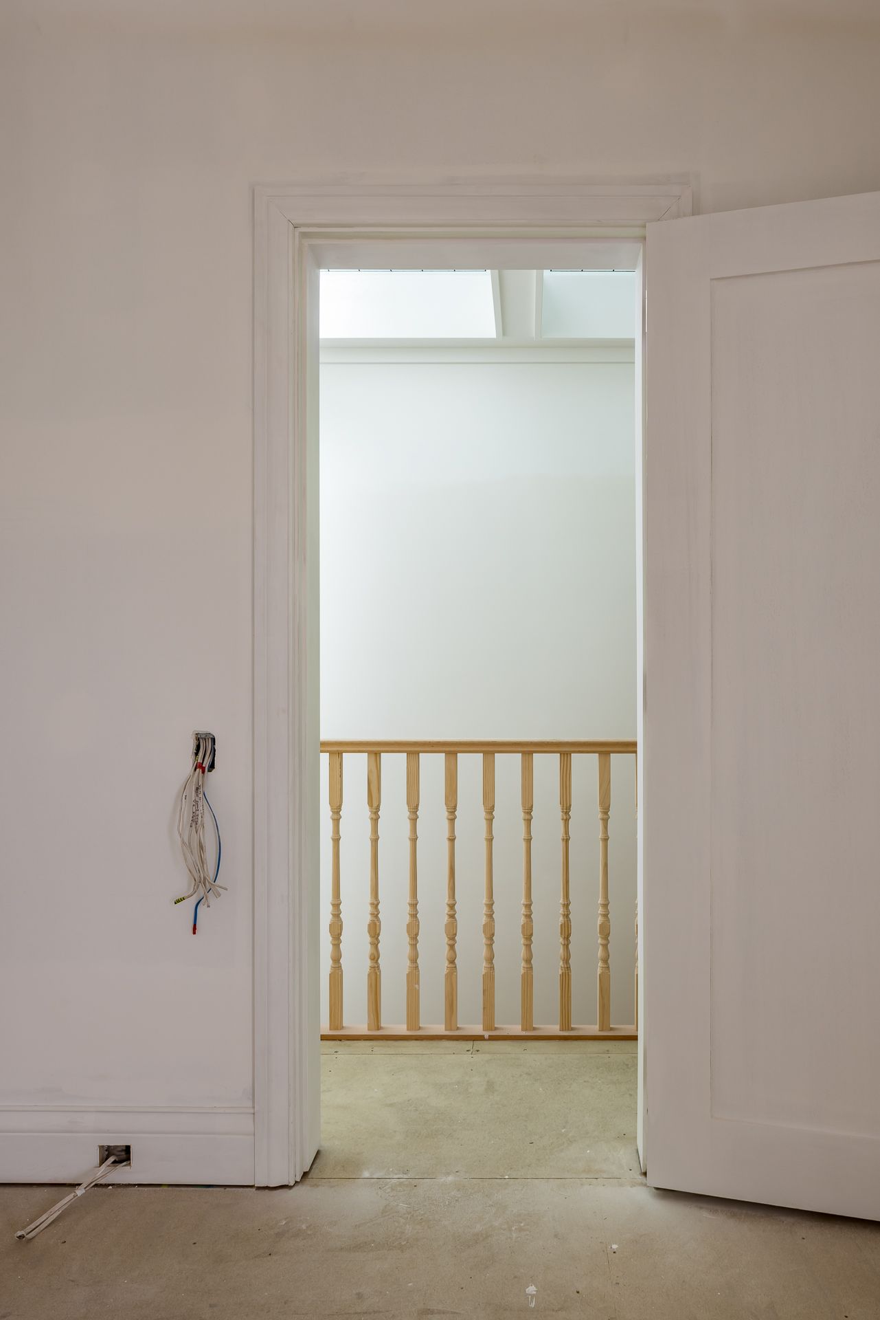 Open white door revealing a timber balustrade and skylight on an upper landing, with loose wiring on the wall.