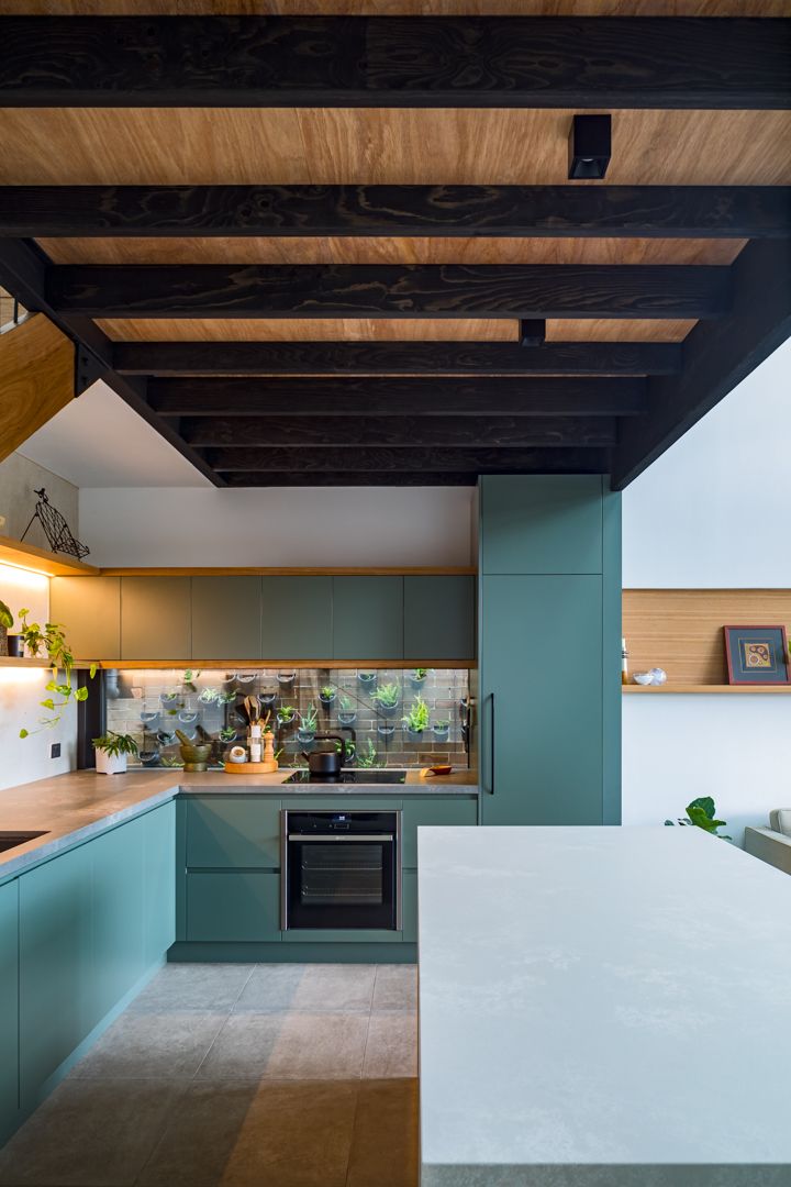 Kitchen with teal green cabinetry, timber benchtops, a dark exposed beam ceiling and a herb-filled splashback.