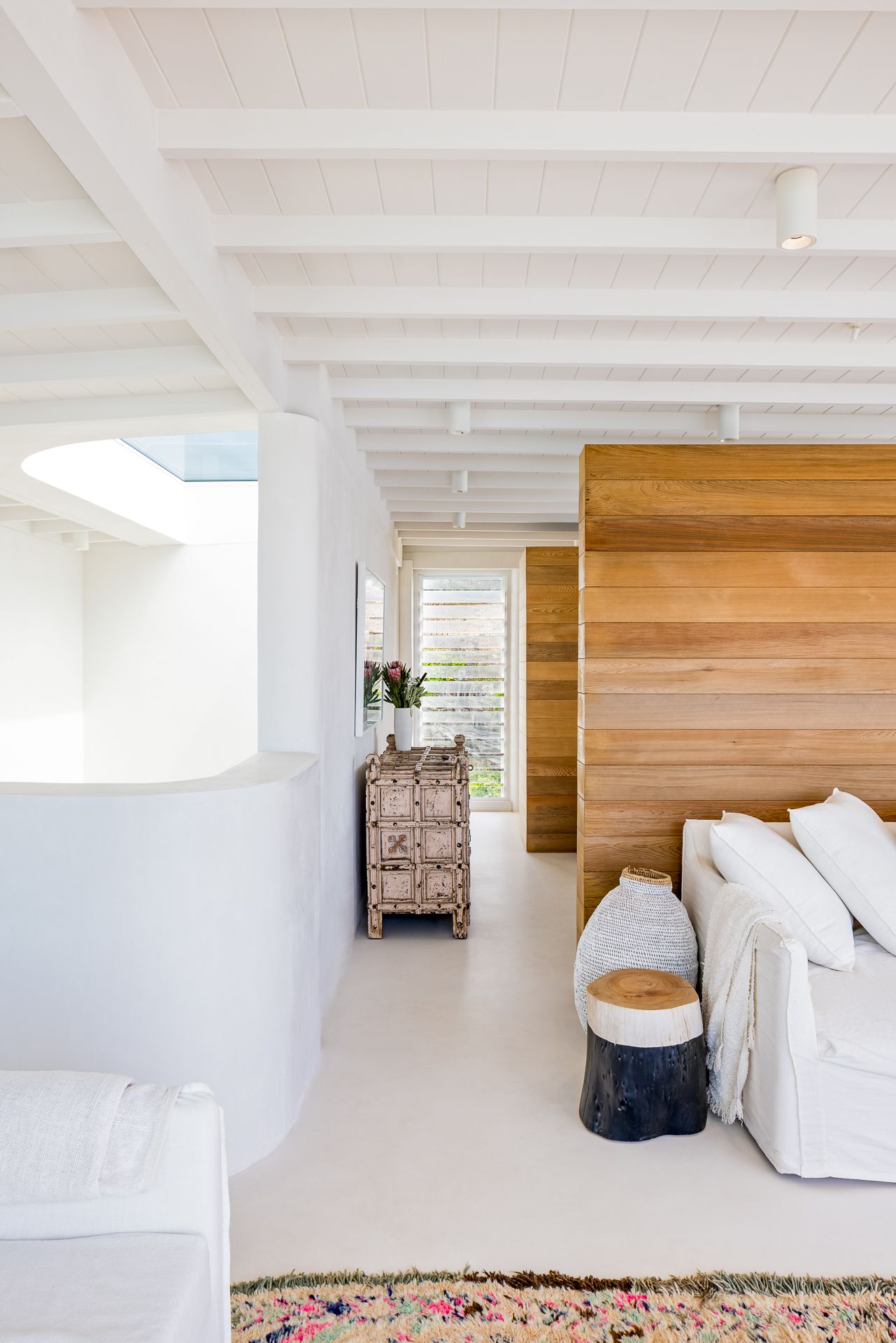 Airy white interior with exposed beams, timber feature wall, white slipcovered sofa, rustic cabinet and fresh flowers.