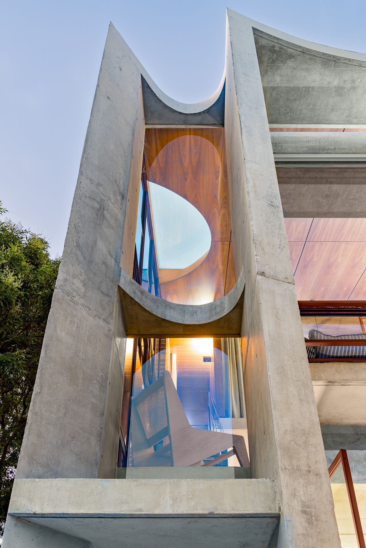 Modern concrete building with curved architectural cutouts framing warm timber interiors and glass windows against a dusk sky.