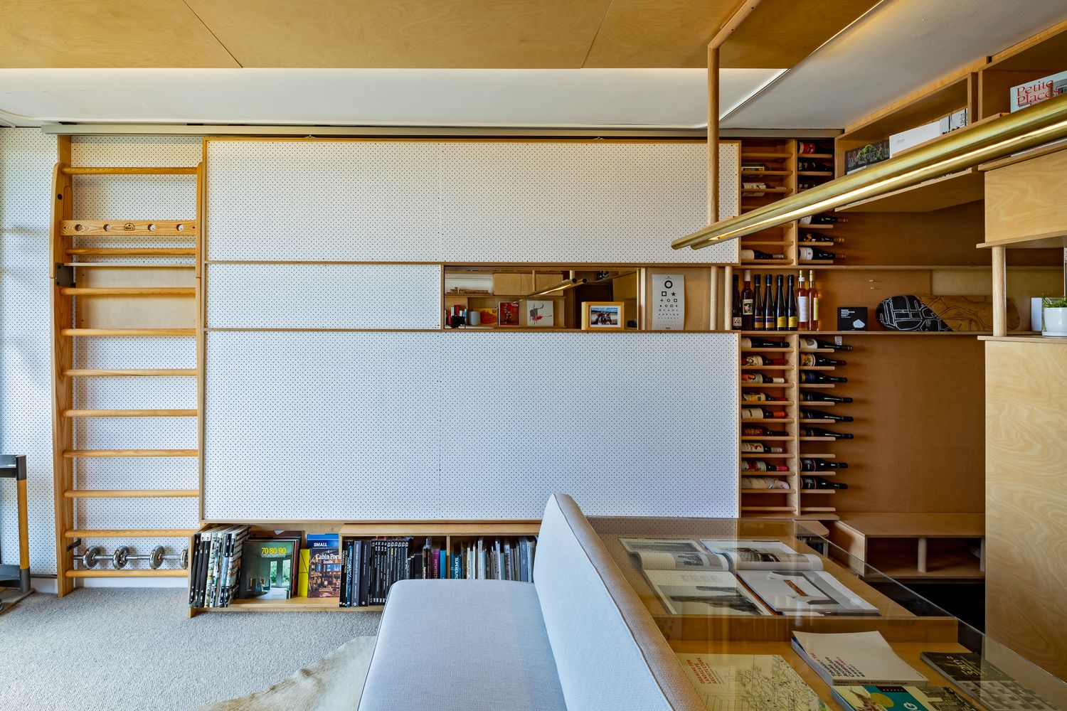 Space-saving apartment interior with wooden wall bars, sliding white panels and built-in shelving beside a sofa.
