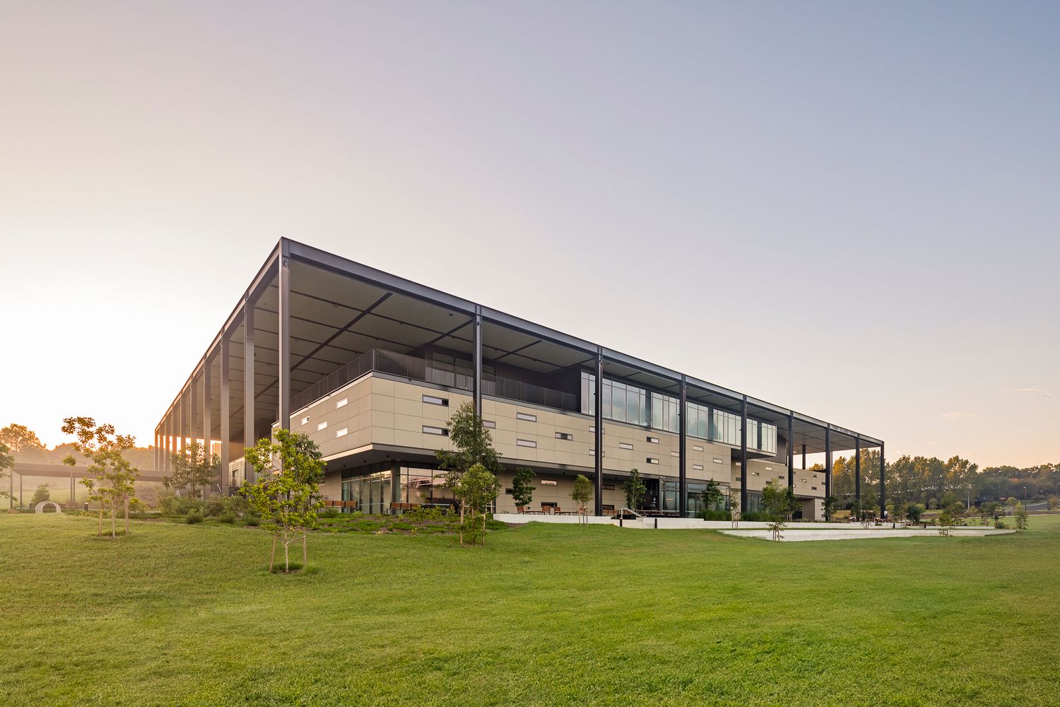 Modern two-storey building with a steel column frame and wide roof overhang set on an open lawn at sunset.