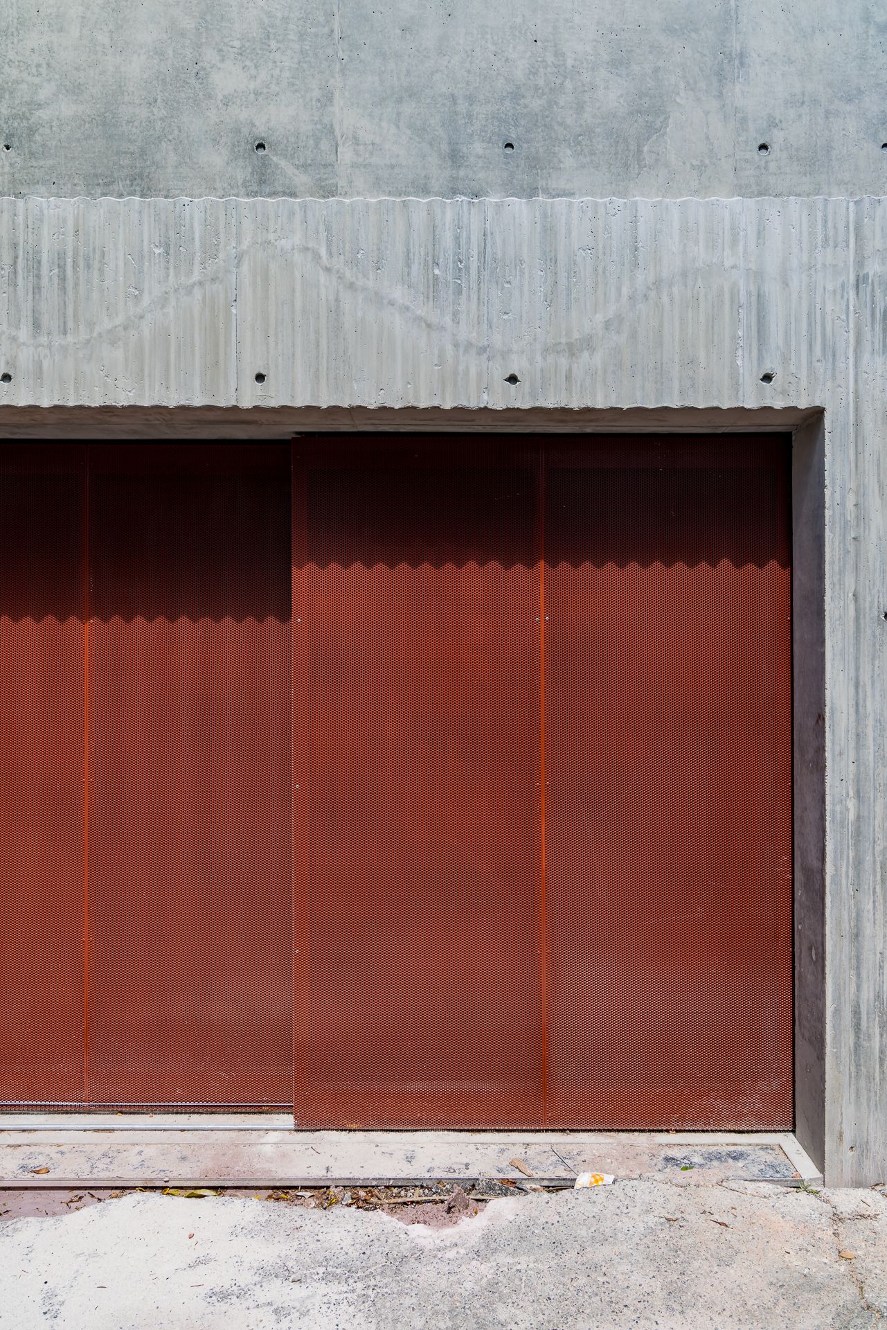 Rust-colored sliding metal garage door set into a board-marked concrete wall above a rough concrete driveway.