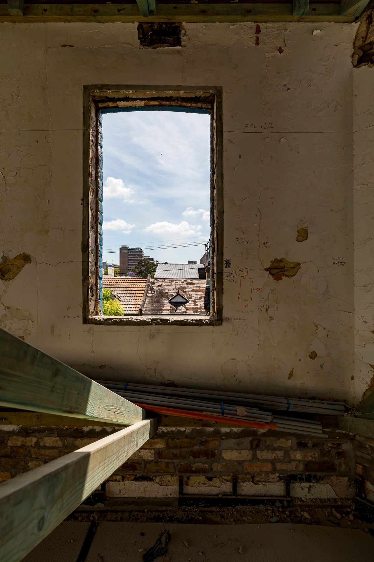 View through an empty window frame in a derelict building with peeling walls, exposed brick and wooden beams, overlooking rooftops and a blu